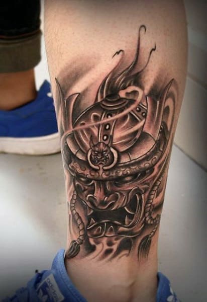 Black and grey calf tattoo of a fierce samurai mask with intricate details, shading, and flowing elements for a dynamic effect