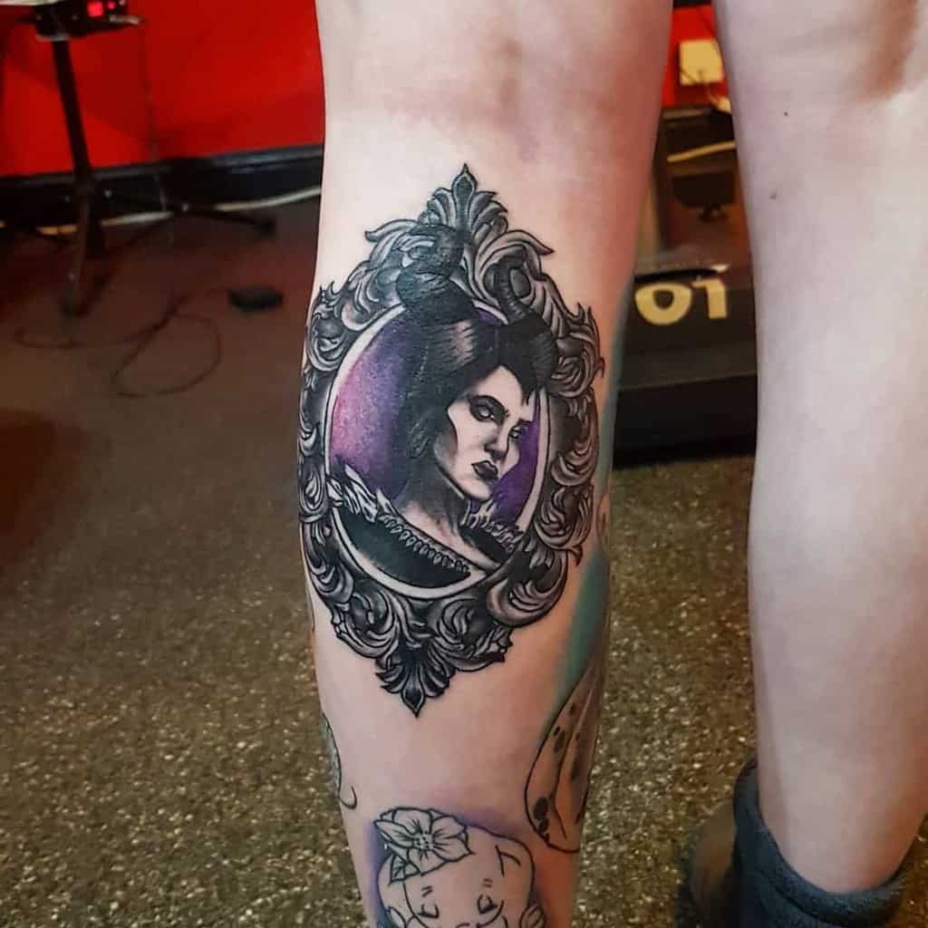 Elegant calf tattoo of Maleficent framed in an ornate mirror, featuring purple hues and intricate black details for a gothic touch
