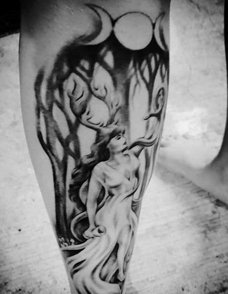 Black and grey calf tattoo of a mystical woman with flowing robes, antlers, and a crescent moon symbol, set against an enchanted forest