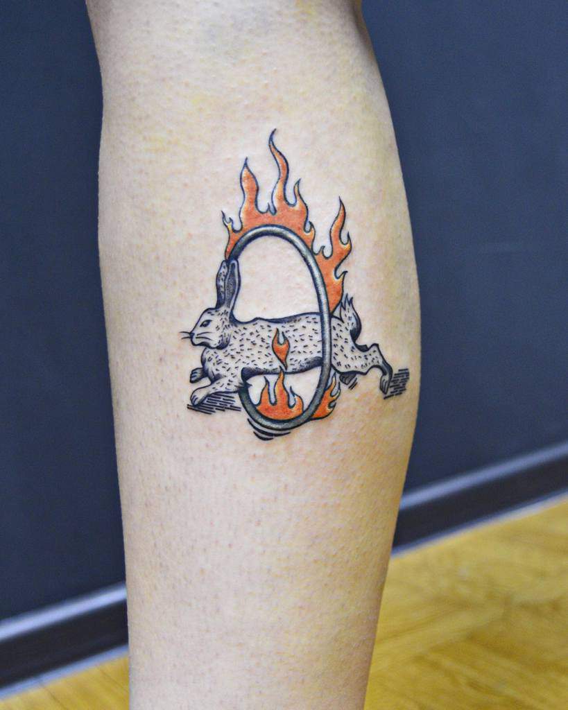 Vivid tattoo of a rabbit jumping through a flaming hoop, with bold black outlines and orange flames