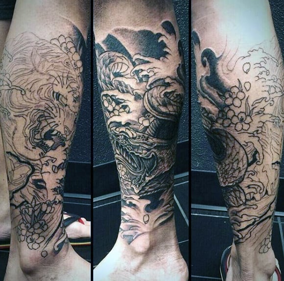Intricate black and grey calf sleeve tattoo featuring a fierce dragon emerging from turbulent waves, with bold shading and dynamic details