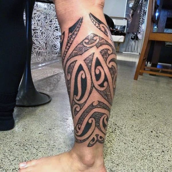 Bold tribal calf tattoo with intricate black ink patterns and swirling designs, wrapping around the leg for a striking look