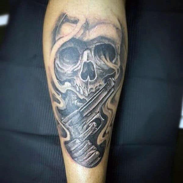 Black and grey calf tattoo of a smoky skull holding a detailed handgun, with intense shading for a bold and dramatic effect