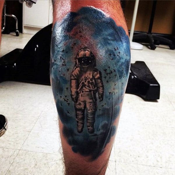 Calf tattoo of an astronaut floating in space, surrounded by a cosmic blue nebula and silhouettes of birds for a surreal effect