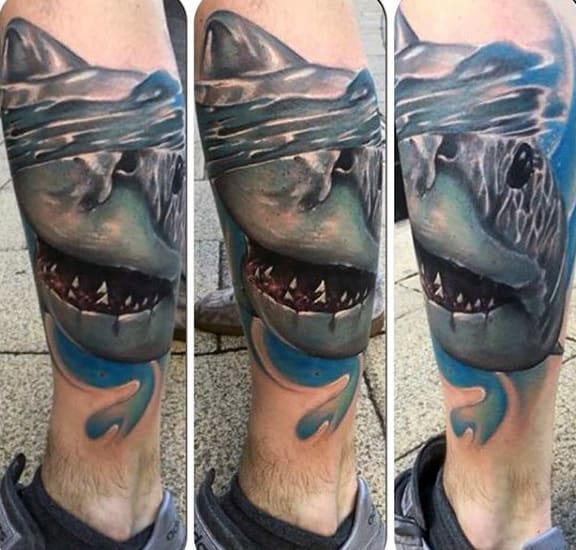 Realistic calf tattoo of a great white shark emerging from the water, with detailed shading and vibrant blue splashes for a dynamic effect