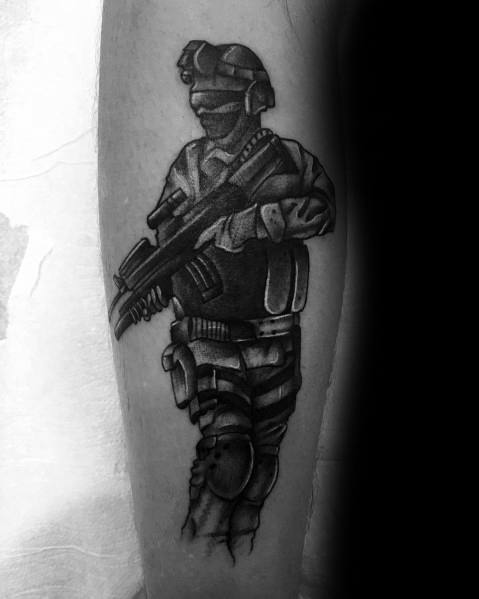 Black and grey Call of Duty soldier tattoo with tactical gear and a rifle, featuring a shadowed face and night vision goggles on the forearm.