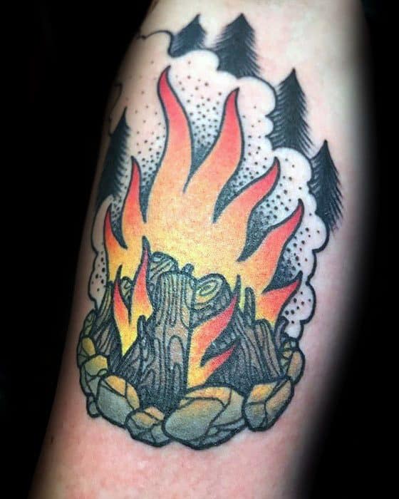 Traditional campfire tattoo with vibrant flames, smoke clouds, stone circle, and pine trees in the background.