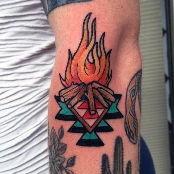 Stylized campfire tattoo with bold flames, crossed logs, and a geometric tribal pattern in red, teal, and black underneath.