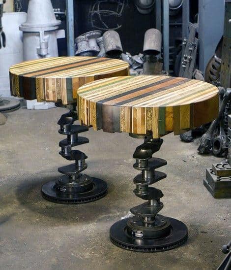 Two round tables with colorful wooden tops and metal bases resembling crankshafts in an industrial setting