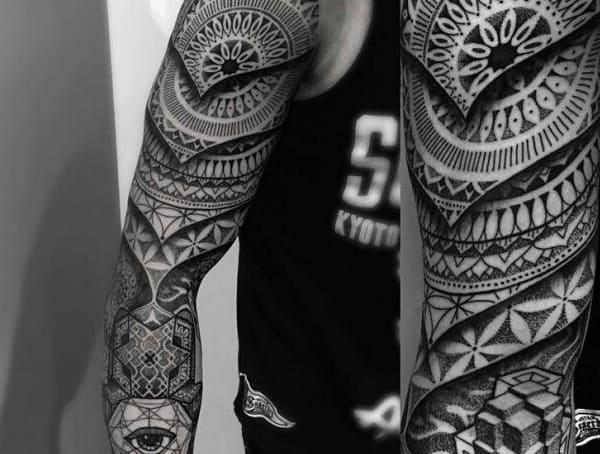 Person with full-arm geometric black and grey tattoos wearing a dark sleeveless shirt