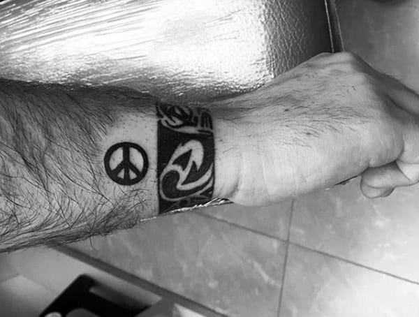 A forearm tattoo featuring a peace symbol and tribal designs in black ink