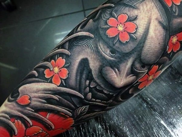 Forearm tattoo featuring a demonic face with red flowers surrounding it