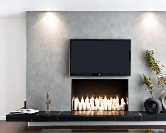 Modern concrete fireplace filled with candles, wall-mounted TV, and minimal decor accents.