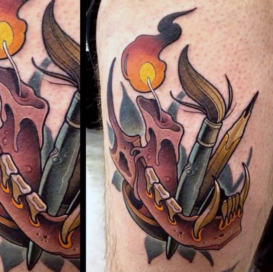The tattoo features a lit candle, paintbrush, and pencil seamlessly intertwined on the skin