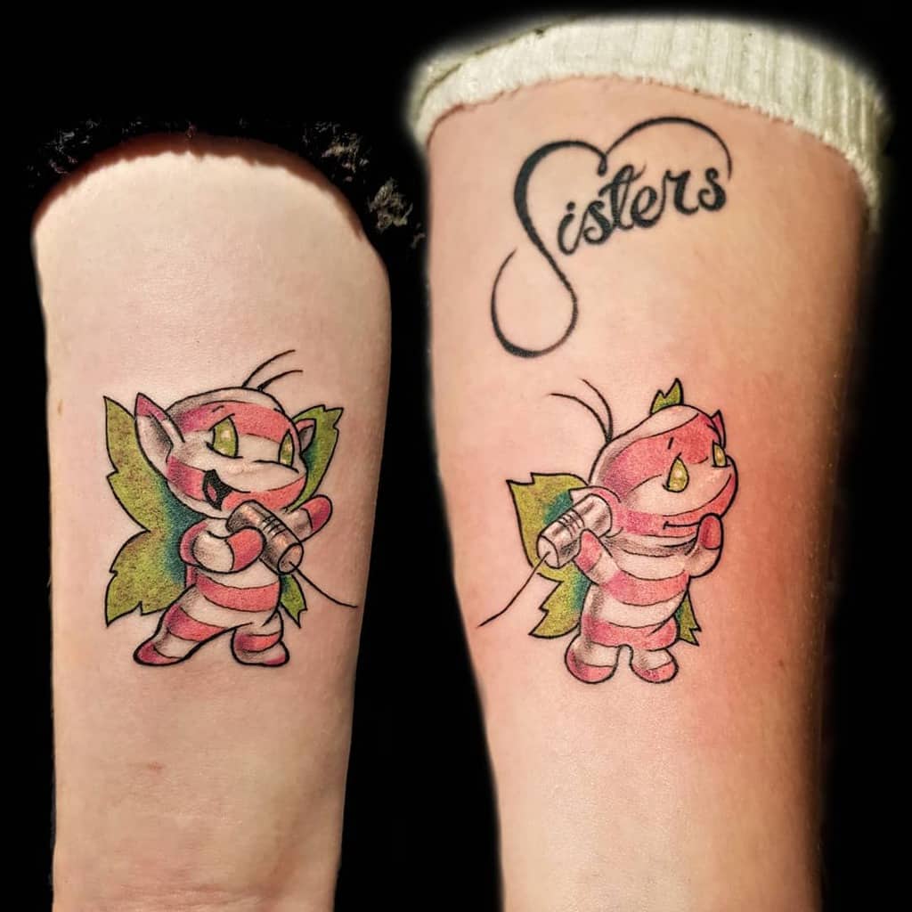 Matching sister tattoos featuring colorful cartoon-style fairies using tin-can telephones, with 'Sisters' elegantly written above one design
