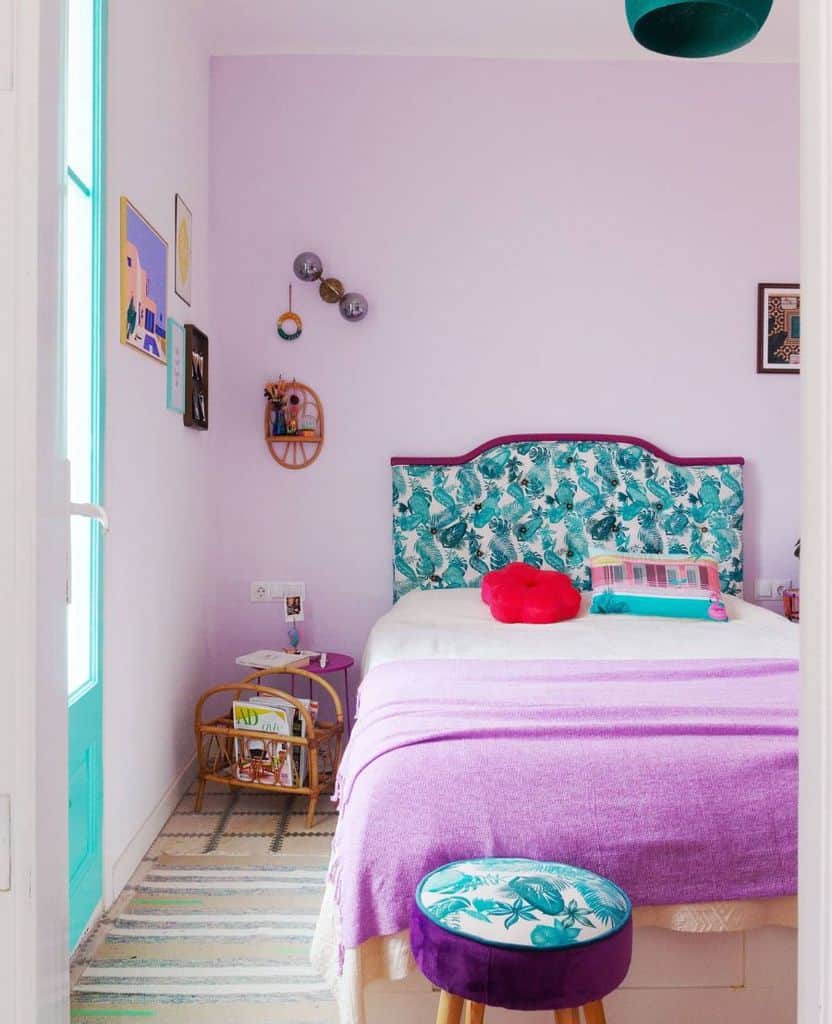A colorful bedroom with a patterned headboard, purple bedding, and eclectic wall art