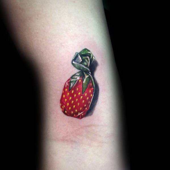 Realistic tattoo of a classic strawberry candy wrapper with detailed shading and highlights, creating a 3D effect on the skin.