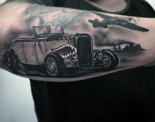 Detailed tattoo of a vintage car with a shark face design and an airplane on a forearm