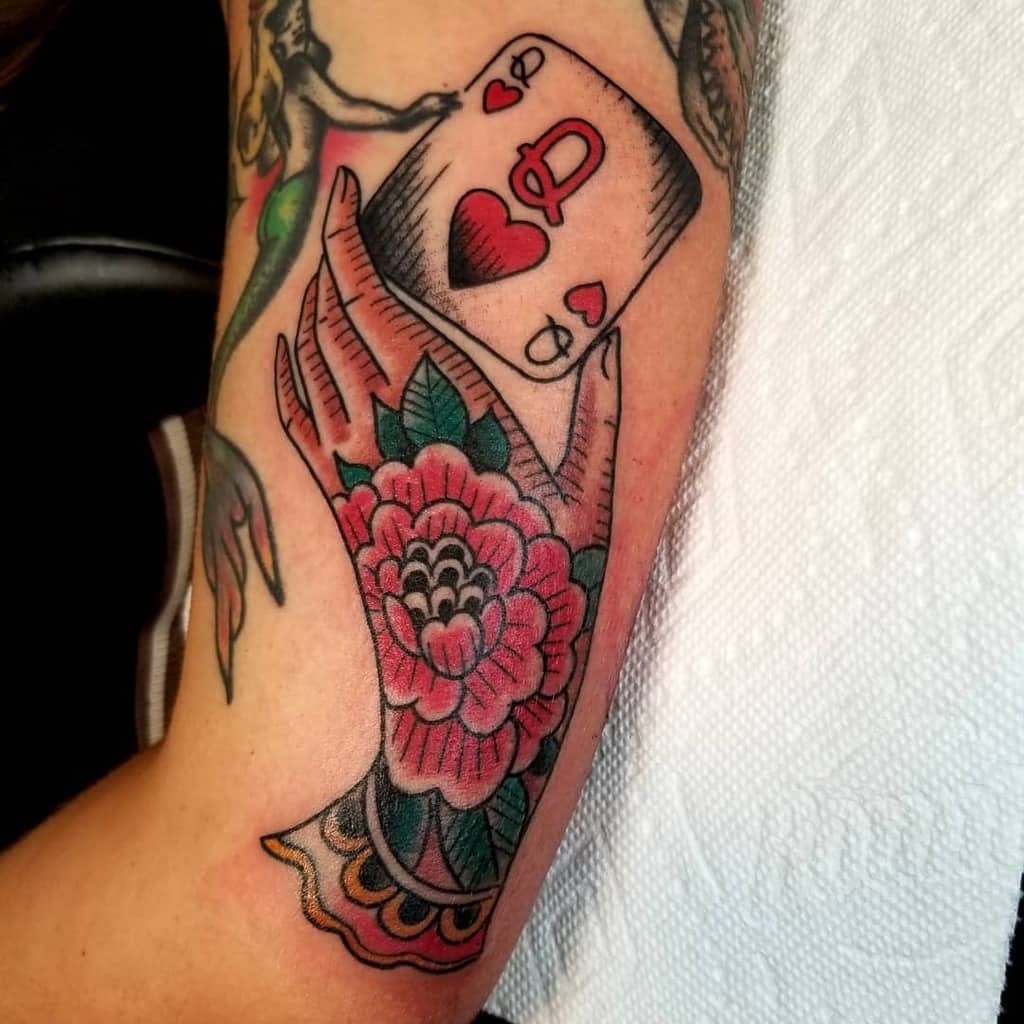 Tattoo of a hand holding the Queen of Hearts card, with floral designs and colorful details