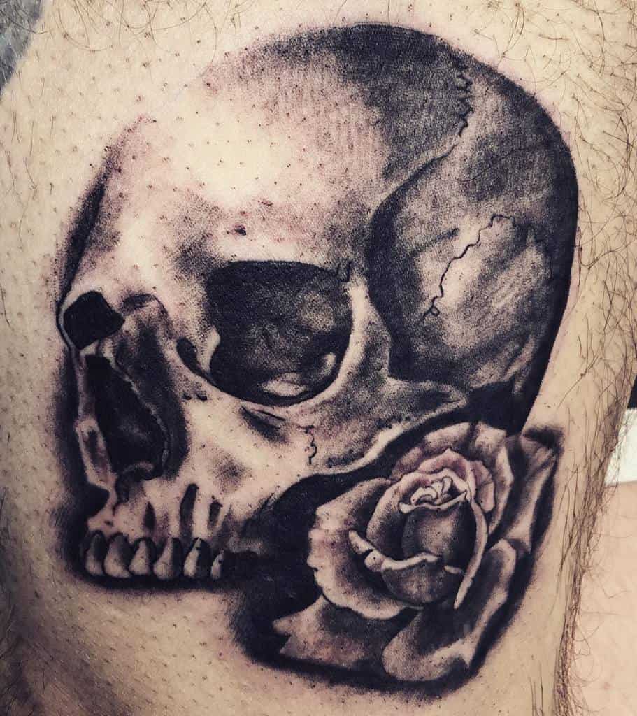 Realistic black and grey tattoo of a cracked skull with a detailed rose, featuring bold shading and intricate textures.