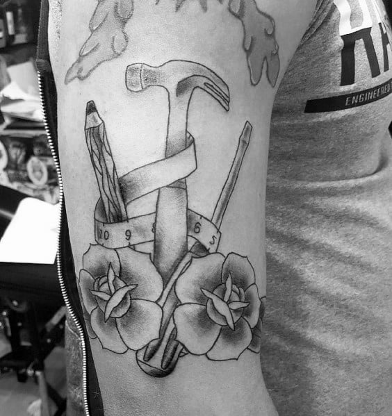 Tattoo of a hammer, pencil, and screwdriver wrapped in a measuring tape, with roses, symbolizing craftsmanship, precision, and creativity.