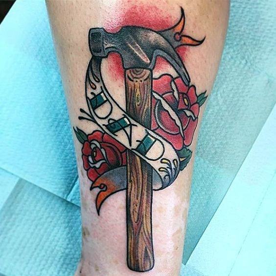 Colorful tattoo of a hammer wrapped in a banner with "DAD," surrounded by roses, symbolizing love, remembrance, and a legacy of craftsmanship.