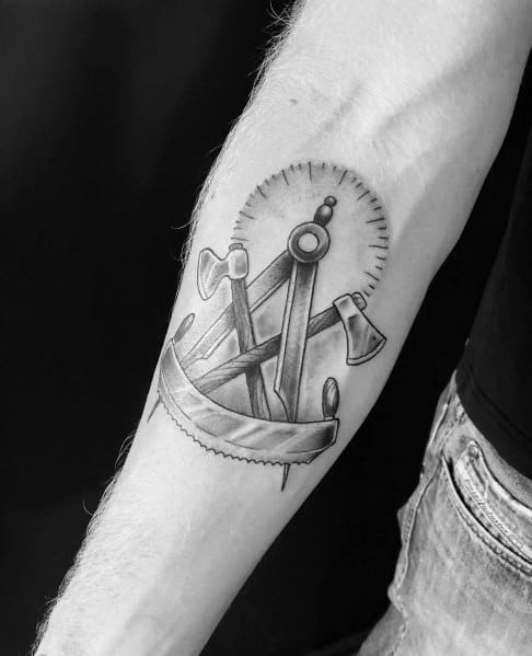 Carpenter tattoo featuring a compass, axes, and a saw blade in black and gray realism on the forearm, symbolizing craftsmanship.
