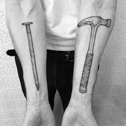 Matching forearm tattoos of a hammer and a nail, representing strength, hard work, and the essence of carpentry and construction.