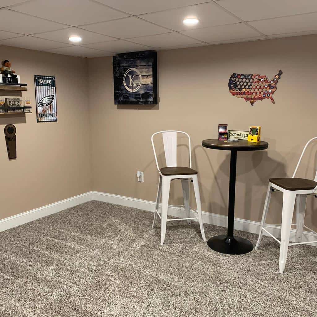 Basement bar area with metal bar stools, round high-top table, and sports-themed wall decor.
