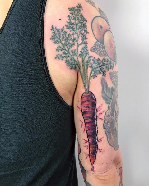 Vibrant carrot tattoo on the upper arm with rich shading, green leafy tops, and red root veins for a bold and artistic organic look.