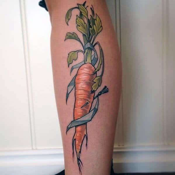 Realistic carrot tattoo on the leg with detailed shading, vibrant green leaves, and a ribbon wrapped around for a bold and artistic design.