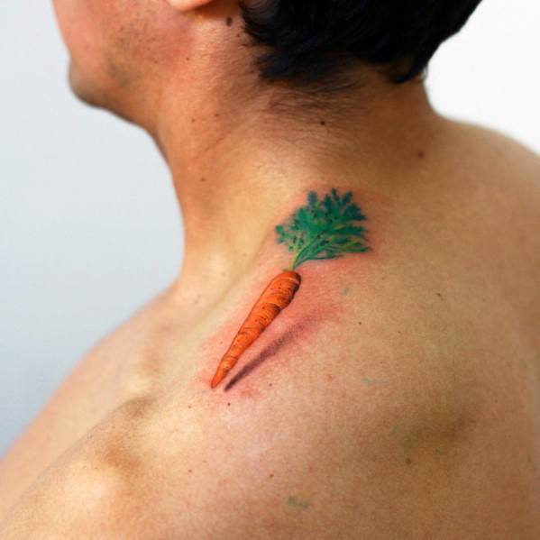 Small and realistic carrot tattoo on the shoulder, featuring vibrant orange and green tones with fine shading for a subtle yet playful design.