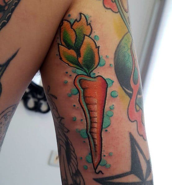 Bold and colorful carrot tattoo on the upper arm with vibrant orange and green tones, surrounded by blue shading for a dynamic, eye-catching look.
