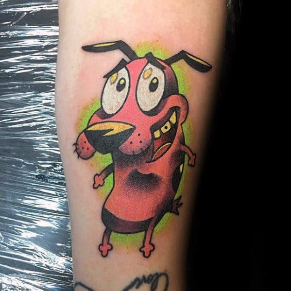 Vibrant tattoo of Courage the Cowardly Dog with a nervous expression, set against a green splatter-style background on the forearm.