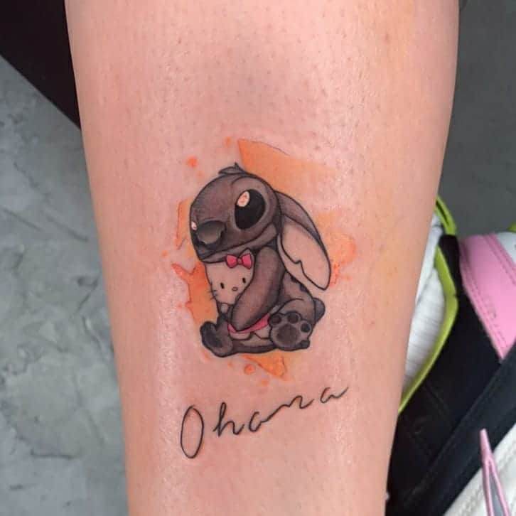 Colorful tattoo of Stitch's sister, Angel, dressed in a bow tie, with the word 'Ohana' written below, on the lower leg.