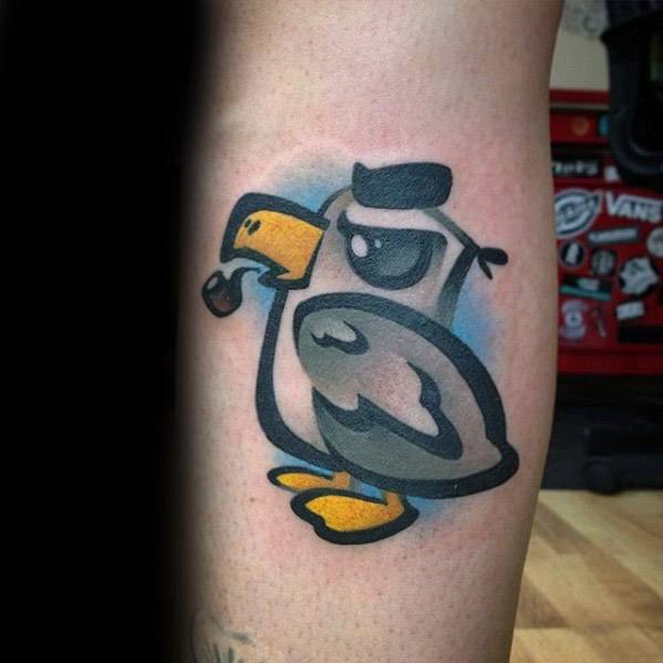 Cartoon-style tattoo of a tough-looking bird with a sailor hat and pipe, featuring bold lines and a splash of blue shading behind.