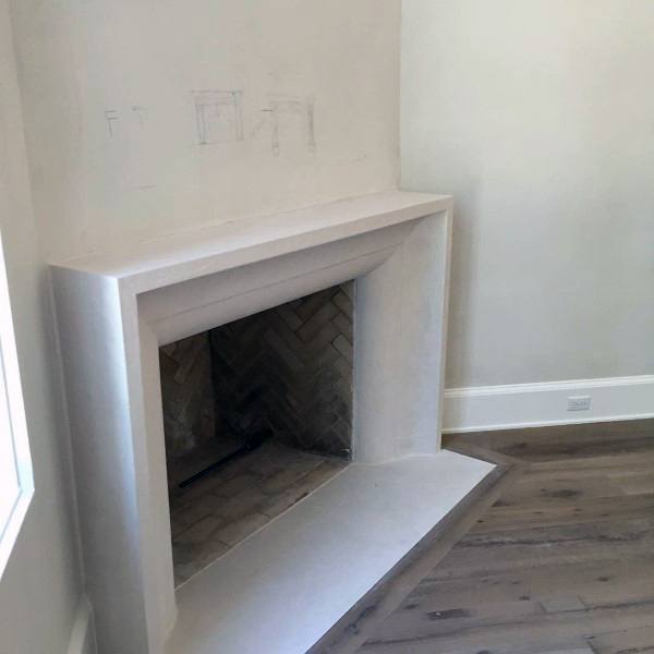 Minimalist cast concrete fireplace with a herringbone brick firebox and smooth contemporary design.