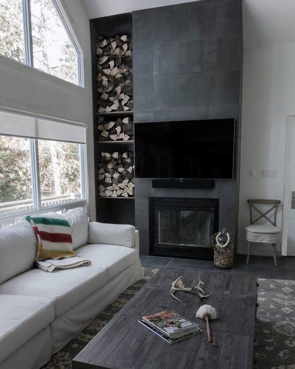 Dark concrete fireplace with built-in firewood storage, mounted TV, and cozy rustic decor.