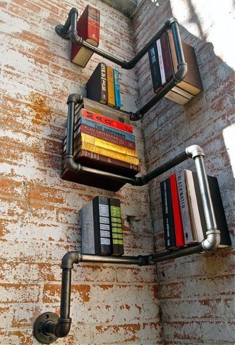 Industrial-style wall-mounted pipe shelves holding books against a brick wall