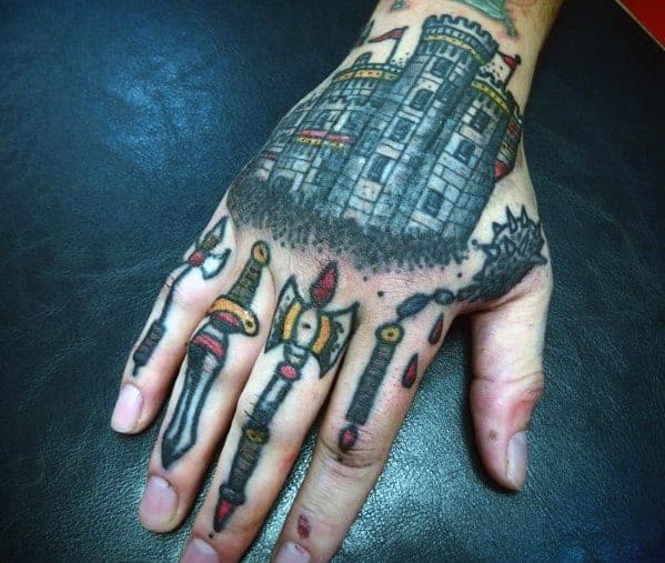 Tattoo of a castle on the back of a hand with dagger designs on the fingers