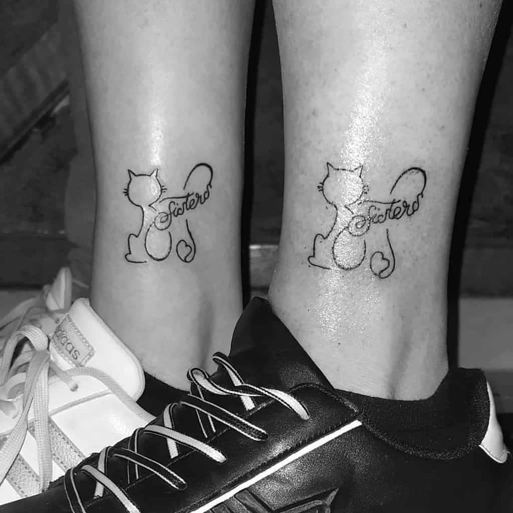 Matching sister tattoos featuring a minimalist cat outline with 'sisters' written in the tail, forming a heart shape