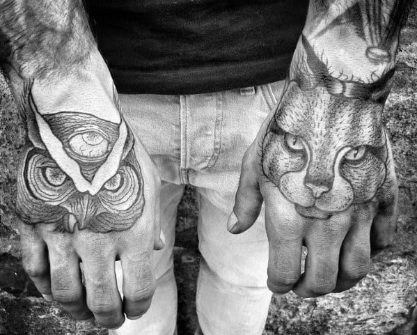 Detailed black and gray hand tattoos featuring a cat on one hand and an owl with a third eye on the other, creating a bold, mystical look.