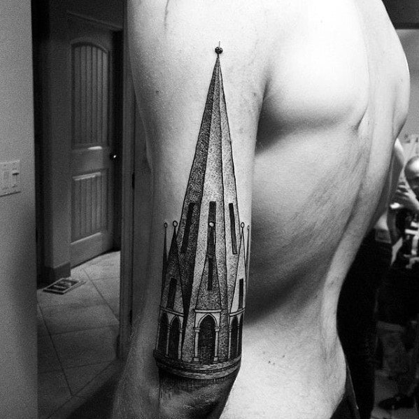 Upper arm tattoo of a tall, narrow gothic cathedral spire with fine dotwork shading and intricate arched window details.