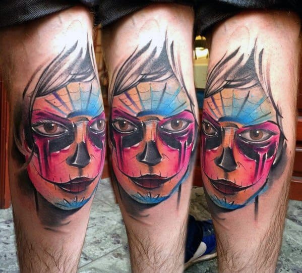 La Catrina tattoo in bold watercolor style, with vivid orange, pink, and blue tones forming a striking sugar skull face on the calf.