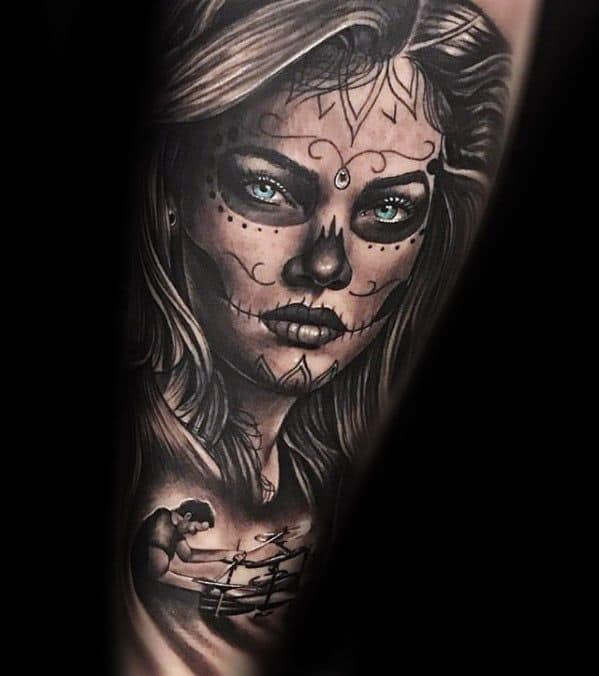 La Catrina tattoo of a woman with teal eyes and sugar skull makeup, featuring a drummer silhouette below in fine black and grey.