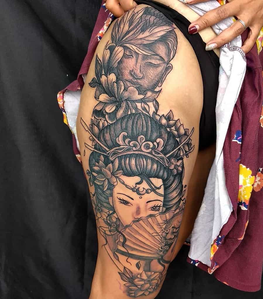 Intricate black and gray thigh tattoo of a Geisha with ornate hair accessories, holding a fan, with a serene Buddha face and floral details above.