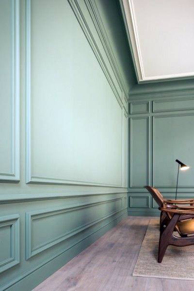 A modern room with elegant green walls, detailed crown molding, and a minimalist chair, creating a stylish and serene atmosphere