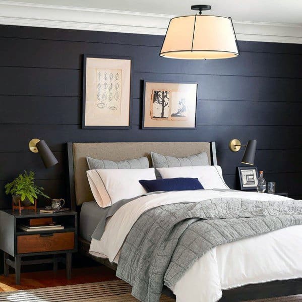 Modern bedroom with black wood paneling, framed wall art, and cozy bedding.