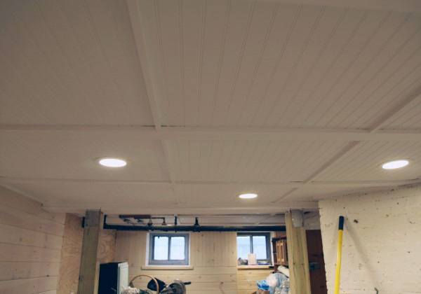 Basement with white shiplap ceiling, recessed lighting, and unfinished wooden walls.