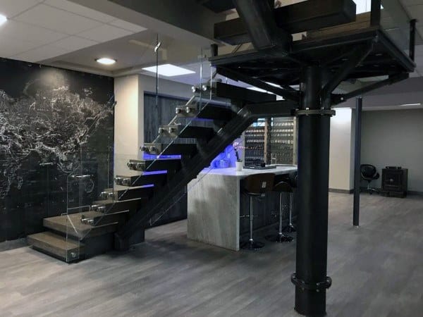 Industrial-style basement with exposed beams, modern staircase, glass railing, and bar area.